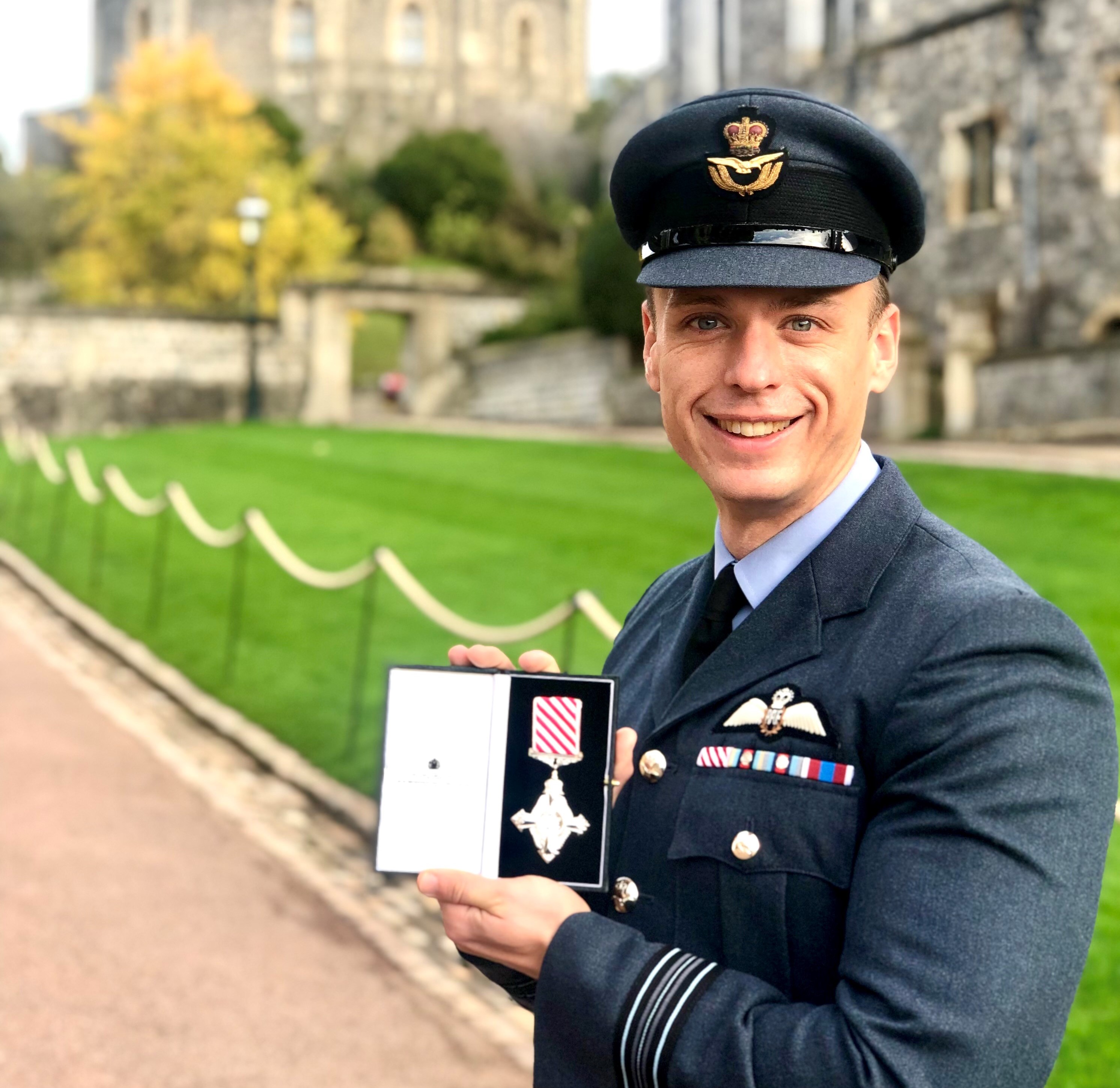 Image shows RAF aviator holding his medal outside Windsor Castle..